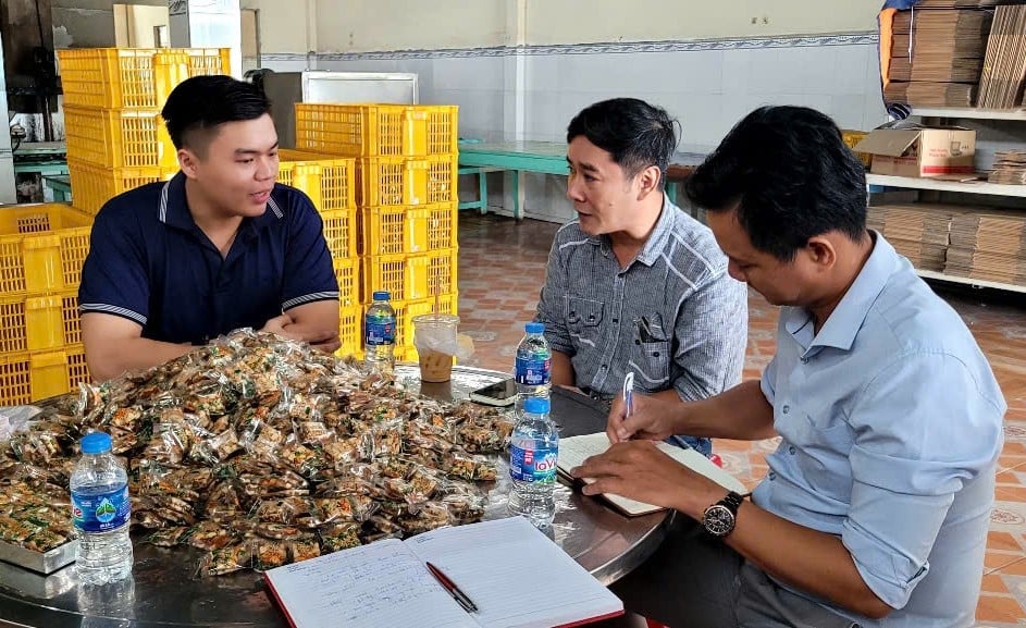 Anh Nguyễn Chí Thiện (bên trái), chủ cơ sở kẹo khóm Tân Phước trao đổi với khách hàng tới tìm hiểu quy trình sản xuất kẹo từ trái khóm. Ảnh: Minh Đảm.