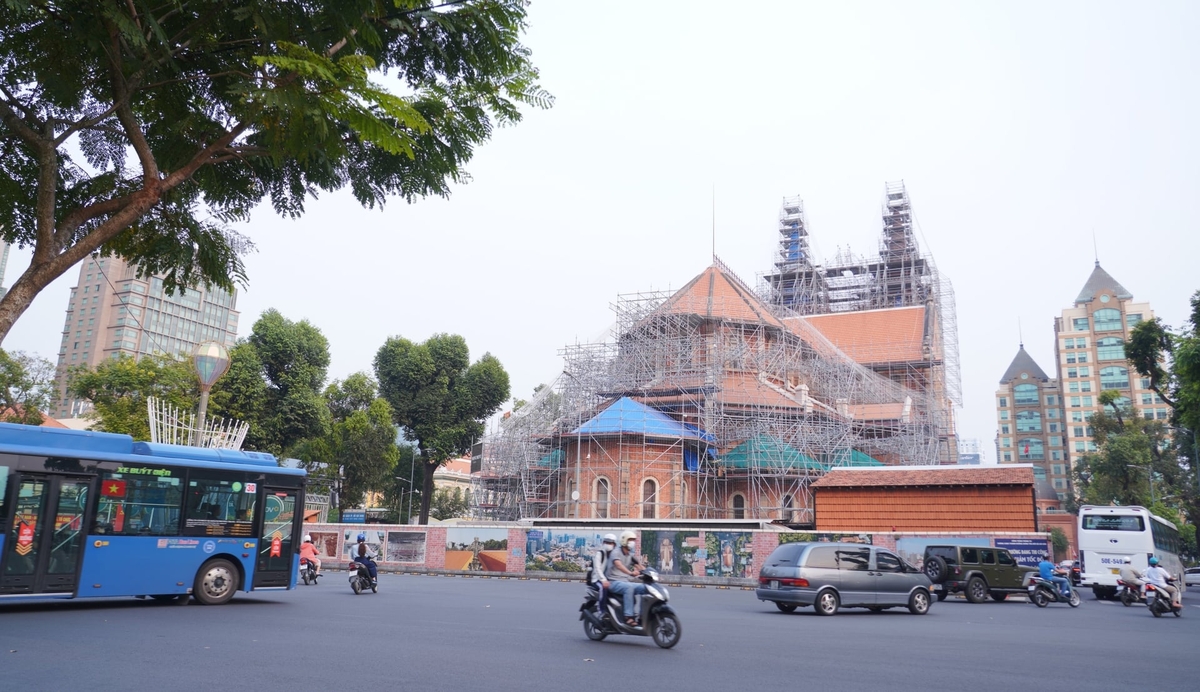 Nhà thờ Đức Bà nhìn từ trục đường trung tâm trong những ngày cận Tết Nguyên đán 2026, khi công trình đang được che chắn, trùng tu giữa dòng xe cộ vẫn lưu thông đều đặn. Ảnh: Trần Phi.