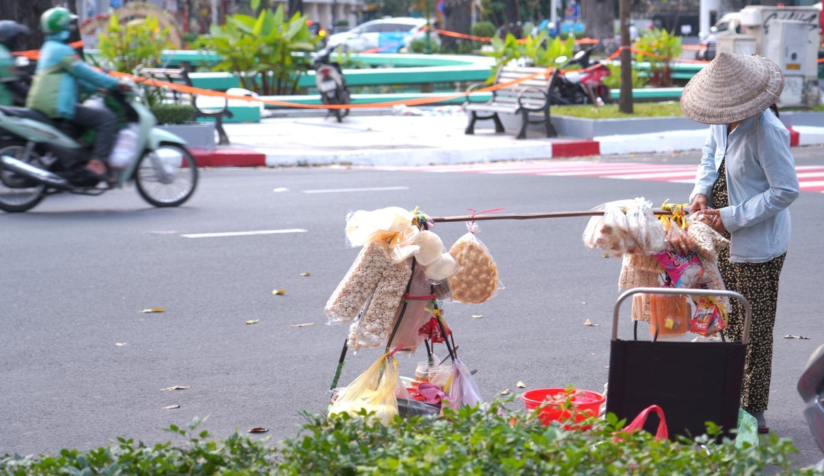 Người bán hàng rong lặng lẽ sắp lại gánh bánh bên Hồ Con Rùa, chọn một góc quen để mưu sinh giữa không gian vừa được chỉnh trang, yên ả hơn thường ngày. Ảnh: Trần Phi.