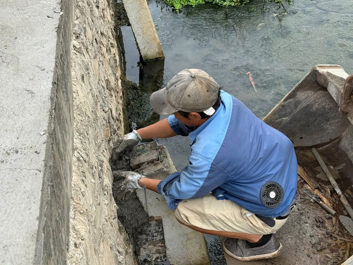Công nhân trám vữa, gia cố đầu cọc bê tông tại khu vực kè giáp kênh nước. Ảnh: Tú Thành.