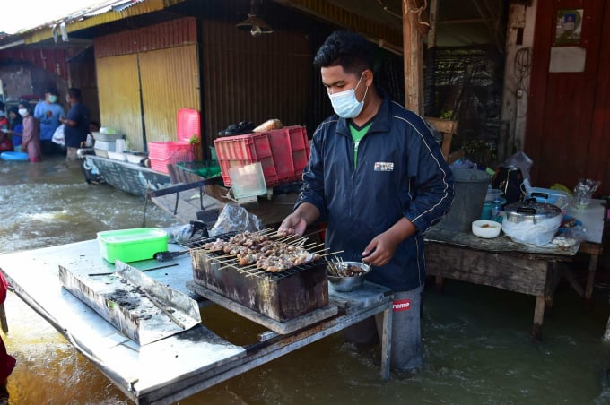 Một người đàn ông chuẩn bị món gà quay đang đứng trong nước lũ sau trận mưa lớn ở tỉnh Narathiwat, miền nam Thái Lan vào tháng trước. Ảnh: AFP.