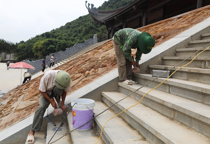 Bức tranh lớn bên ngoài sảnh chùa đang được các công nhân hoàn thiện dưới tiết trời nắng nóng đầu hè.