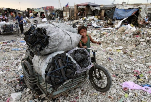 Cậu bé đẩy xe chất đầy than củi, khó khăn khi đi qua một bãi rác trên đường ở Tondo, Phillipines.