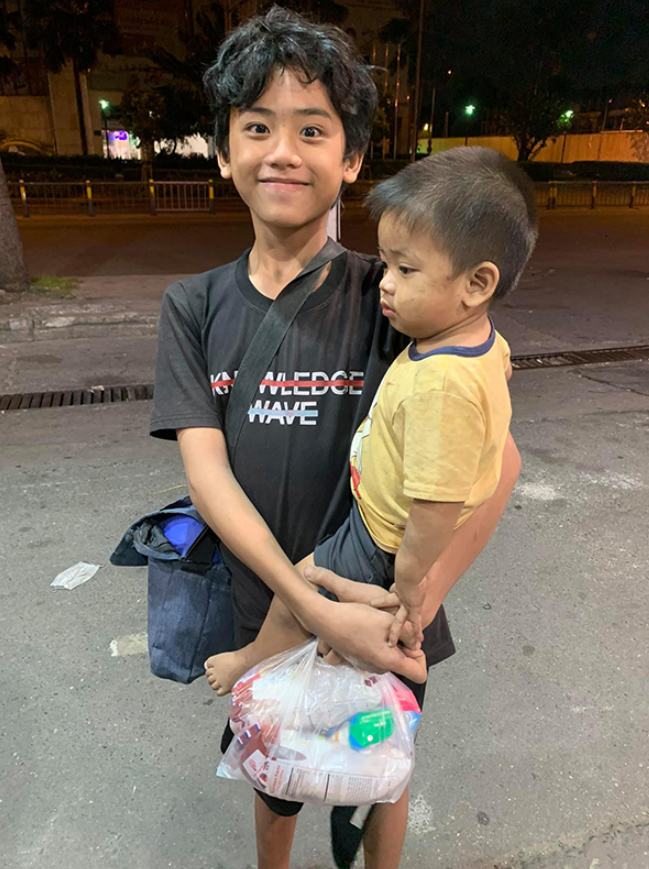 Nụ cười rạng rỡ của Cường khi bồng trên tay đứa em 1 tuổi rong ruổi xin ăn khắp Sài Gòn vì thương mẹ. Ảnh: Facebook.