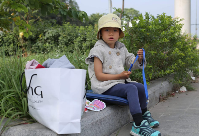 Bé Trang ngồi chơi ngoan trong công viên trong khi bố bán hàng.