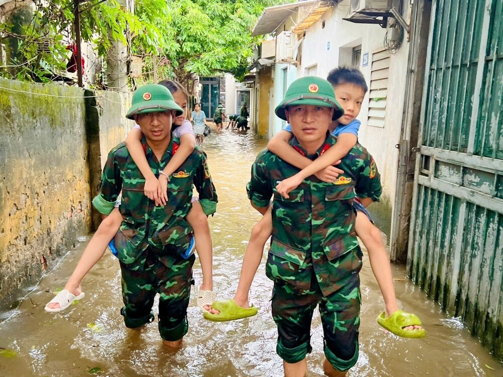 Lực lượng quân đội ngâm mình trong nước giúp dân di dời đến nơi an toàn. Ảnh: Bảo Thoa.