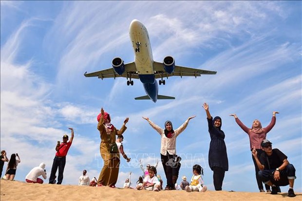 Tourists pose for a picture on Mai Khao Beach in Phuket as a plane lands at Phuket International Airport. Photo courtesy of AFP.