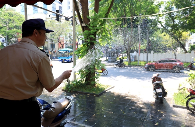 A man sprays water to ease heat on the ground in Hanoi. Photo courtesy of Vietnam News Agency.