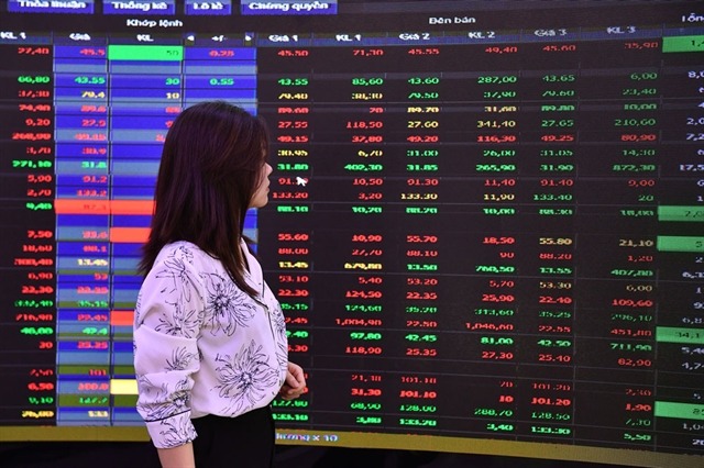 A woman passes an electric board showing share movements. Photo courtesy of VietNamNet.