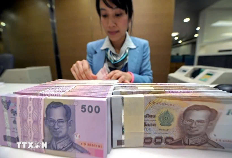   A bank teller counts baht notes in Bangkok, Thailand. Photo courtesy of AFP/VNA.