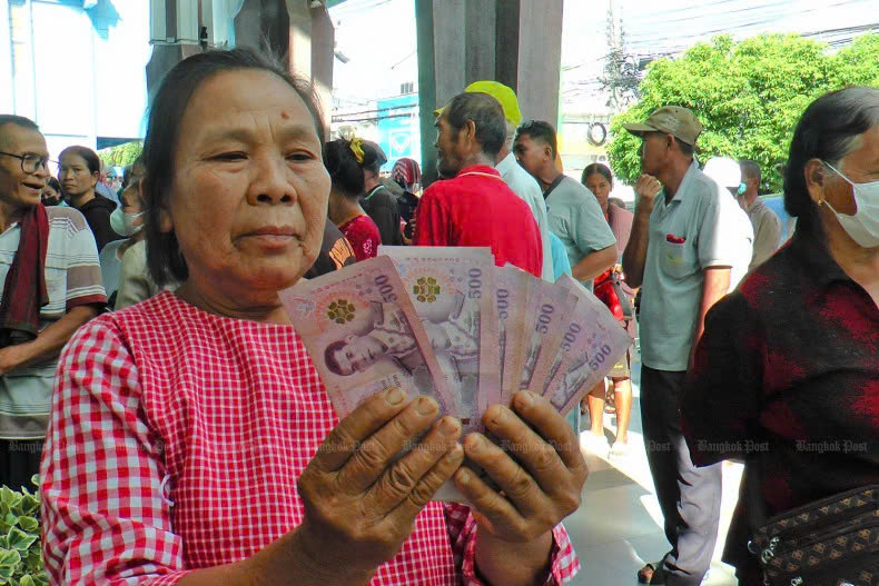  A woman holds up her share of the 10,000-baht cash handout, which is deemed part of the government's economic stimulus plan. Photo courtesy of Bangkokpost.