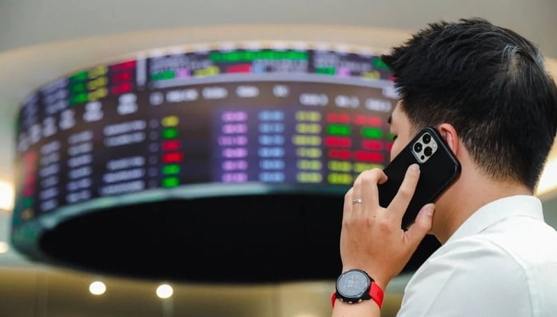An investor talks on a mobile phone in front of an electronic board displaying Vietnamese stock prices. Photo by The Investor/Trong Hieu.