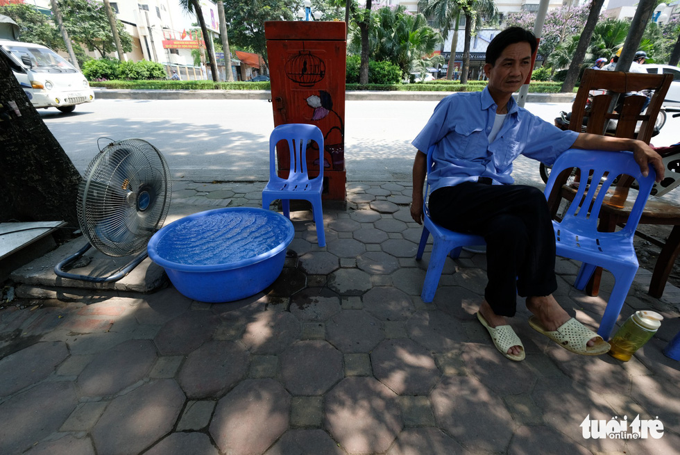 Một nhân viên bảo vệ trên đường Hoàng Quốc Việt, Hà Nội đặt chậu nước lớn trước quạt để bớt cái hấp nóng từ mặt đường - Ảnh: NAM TRẦN