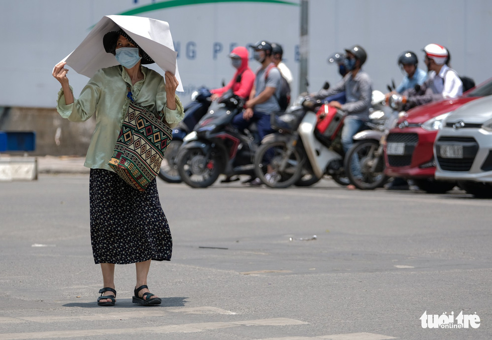 Một phụ nữ che tấm bìa giấy trên đầu khi qua đường dưới thời tiết oi nóng giữa trưa - Ảnh: NAM TRẦN