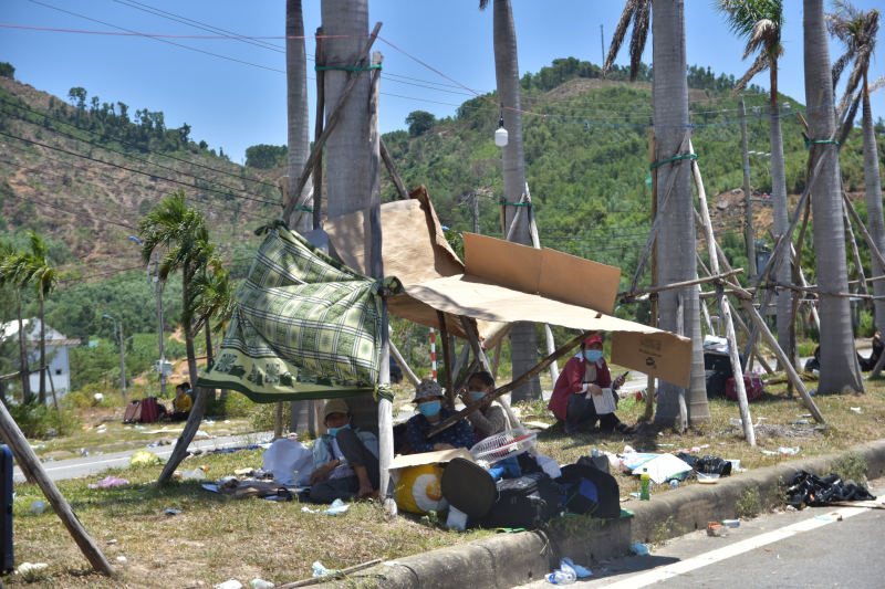 Dưới thời tiết nắng nóng, nhiều người dân dùng các tấm màn, bạt... che chắn, nghỉ chân bên lề đường. Nhiều gia đình có con nhỏ và tất cả mọi người có vẻ mệt mỏi.