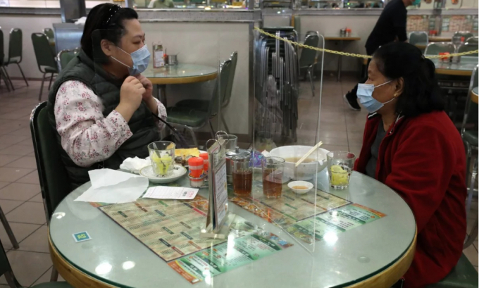Hai thực khách quen biết nhau được ngăn cách bằng một tấm nhựa tại một nhà hàng ở Cửu Long, Hong Kong.