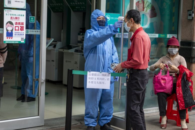 Một nhân viên bảo vệ đeo khẩu trang và đồ bảo hộ kiểm tra nhiệt độ của khách tại lối vào ngân hàng ở Quảng Châu hôm 24/2.