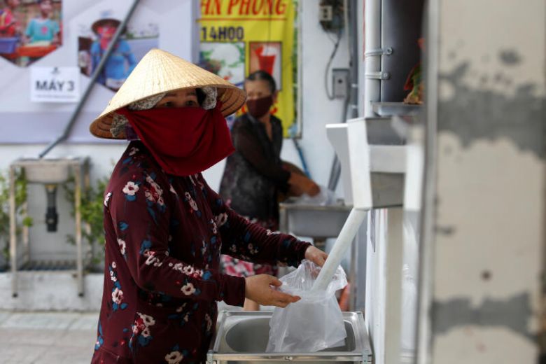 Một người phụ nữ hứng gạo từ máy rút gạo tự động 24/7 tại Hồ Chí Minh hôm 11/4. Ảnh: Reuters.