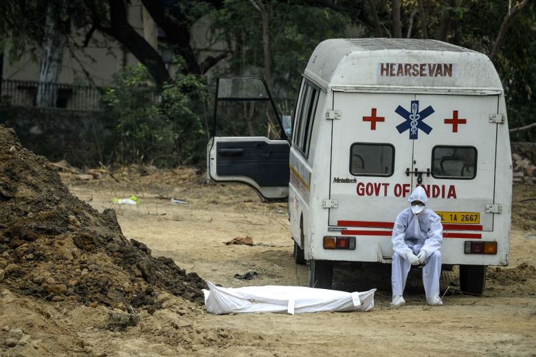Một nhân viên y tế ngồi trên xe cứu thương bên cạnh thi thể nạn nhân Covid-19 chuẩn bị được chôn cất tại một nghĩa địa ở New Delhi hôm 13/5.