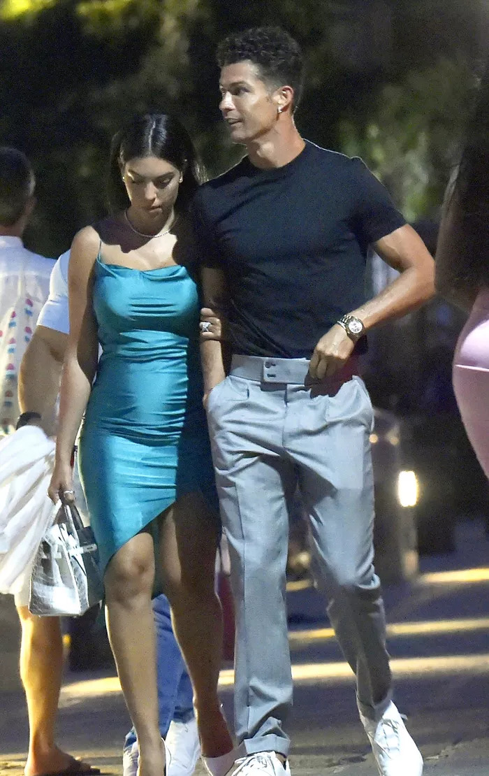 Tiền đạo Juventus diện trang phục thu hút với quần dài màu xám và áo phông xanh. Trong khi đó, Georgina mặc chiếc đầm bó sát màu xanh.