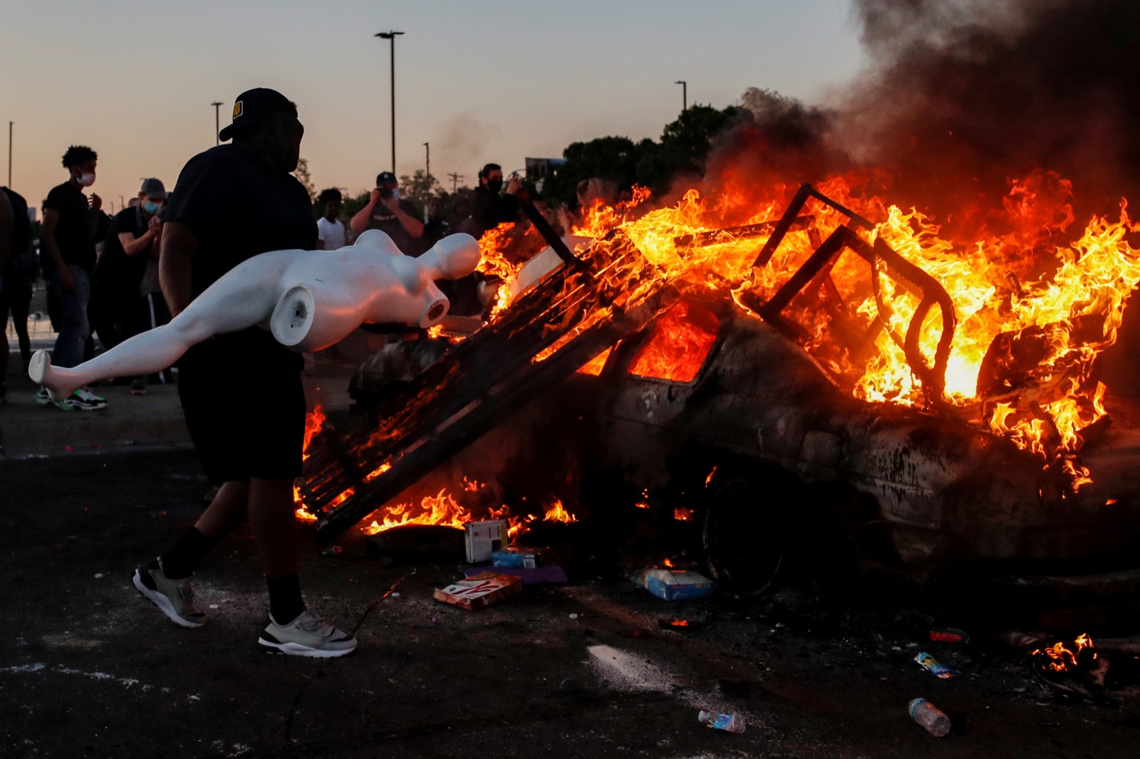 Một người đàn ông chuẩn bị ném con ma nơ canh vào chiếc ô tô bị đốt cháy trong bãi đỗ xe của một cửa hàng ở Minneapolis. Ảnh: REUTERS/Carlos Barria