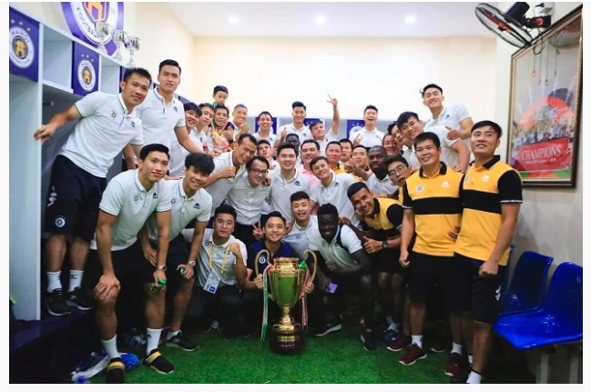 BLĐ và các cầu thủ Hà Nội FC bên chiếc cúp Quốc Gia trong phòng thay đồ (ảnh fanpage Hà Nội football Club)