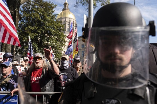 Một sĩ quan trong trang phục chống bạo động đứng giữa những người ủng hộ Tổng thống Donald Trump. Ảnh: AP.