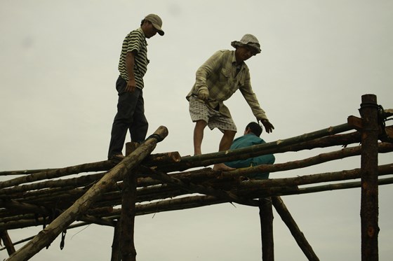 Phía trên giàn cầu, những người đàn ông đang sắp xếp lại tre, ván để khung cầu vững chắc