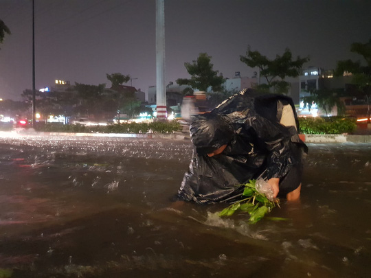 Người dân nhặt rác ở miệng hố ga trên đường Phạm Văn Đồng (quận Bình Thạnh, TP HCM) trong cơn mưa tối 19-5 để nước rút nhanh hơn