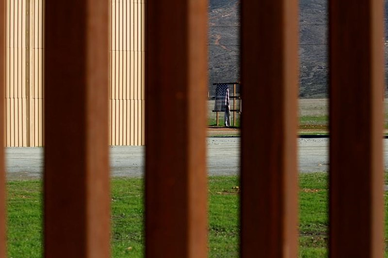 Nhìn qua khe hàng rào biên giới có thể thấy được bản mô phỏng bức tường biên giới cao 9m mà Tổng thống Trump muốn xây dựng.