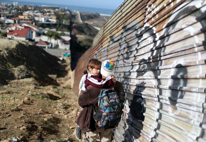 Người di cư từ Honduras đi bộ dọc hàng rào mà họ mong muốn vượt qua để tới Mỹ.