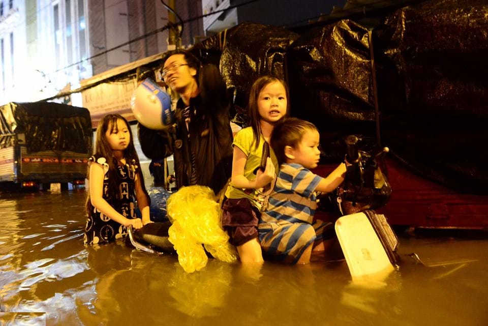 Nước ngập gần quá yên xe khiến người cha và những đứa trẻ bị kẹt lại giữa đường. Ảnh: Lê Quân    