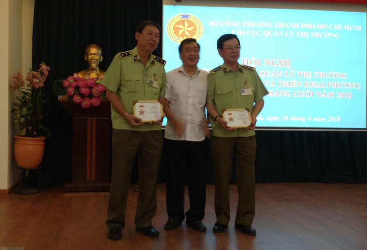 Giám đốc Sở Công thương TP.HCM (giữa) tặng kỷ niệm chương của Bộ Công thương cho hai đại diện Chi cục QLTT TP.HCM.