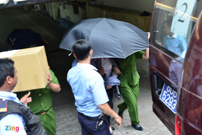 Cảnh sát áp giải một người phụ nữ bị còng tay, che mặt ra xe (ảnh: Zing.vn).