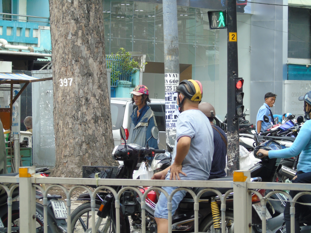 Người đàn ông đứng xin tiền tại điểm dừng đèn đỏ trên Nguyễn Trãi,Q1. Trên tay là điếu thuốc nghi ngút khói, chỉ đợi đèn đỏ là xuống đường để xin tiền.