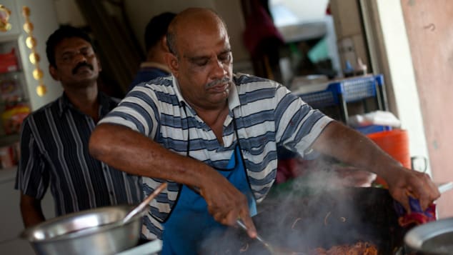 Một người đàn ông đang chế biến món mee goreng mamak nổi tiếng với mì vàng, thịt bò hoặc thịt gà, tôm, nước tương, rau và trứng