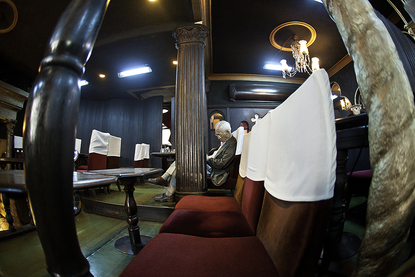 Nội thất của quán cà phê được chiếu sáng lờ mờ, nổi bật với gỗ tối màu và các bức phù điêu chạm khắc