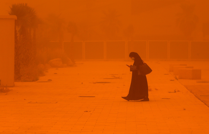 Người phụ nữ chăm chú xem điện thoại khi đi bộ trong cơn bão bụi nghiêm trọng ở thành phố Kuwait