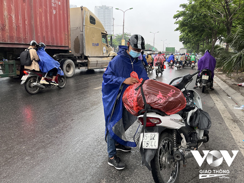 Một người đàn ông dừng xe, buộc lại túi đồ để tránh mưa trước quãng đường dài trước cửa ngõ phía Nam của Thủ đô