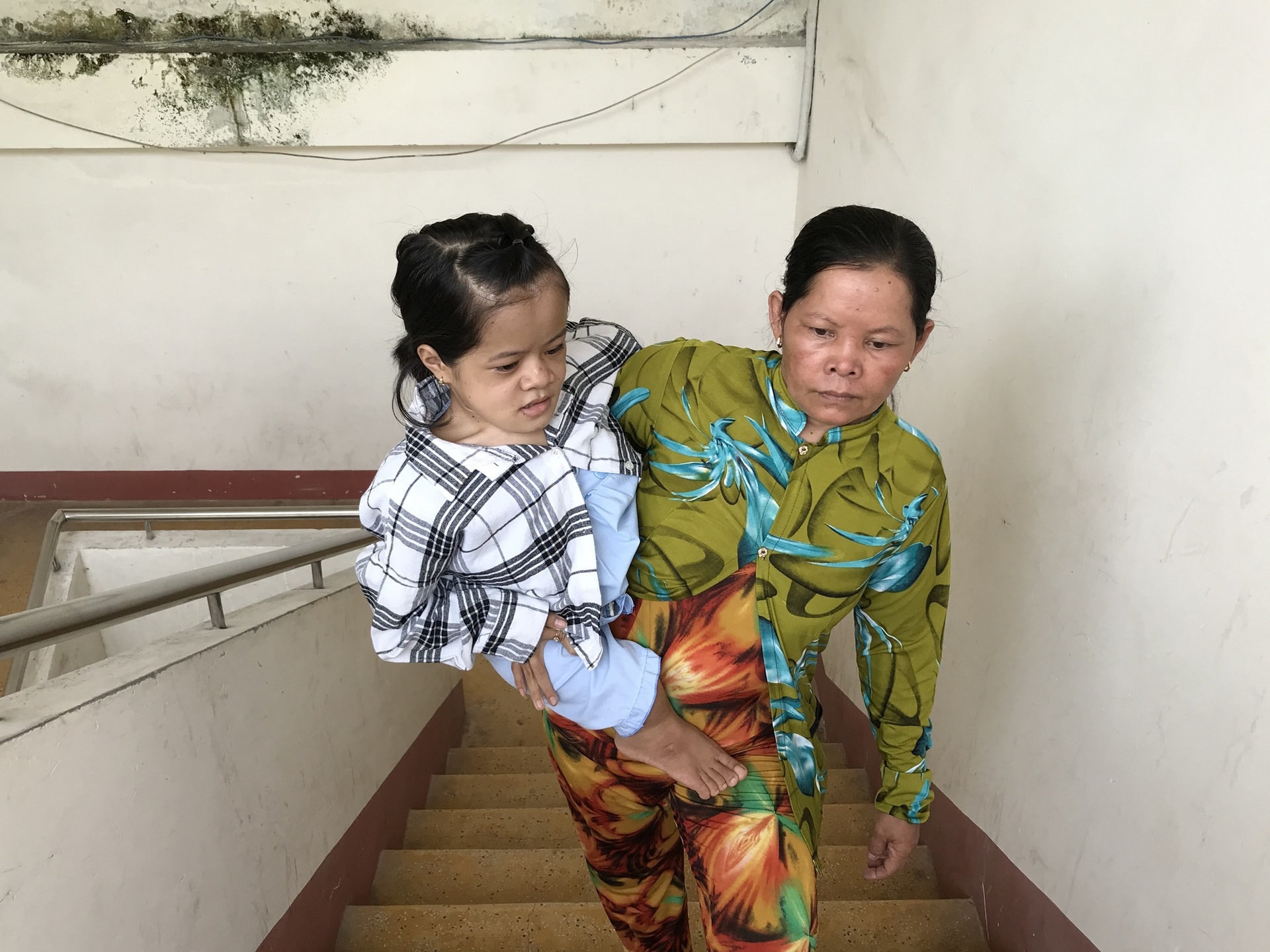 Mỗi ngày, bà Ly, mẹ của Nhí đều đặn bế con vượt qua những bậc cầu thang để đến lớp học - Ảnh Báo Thanh Niên