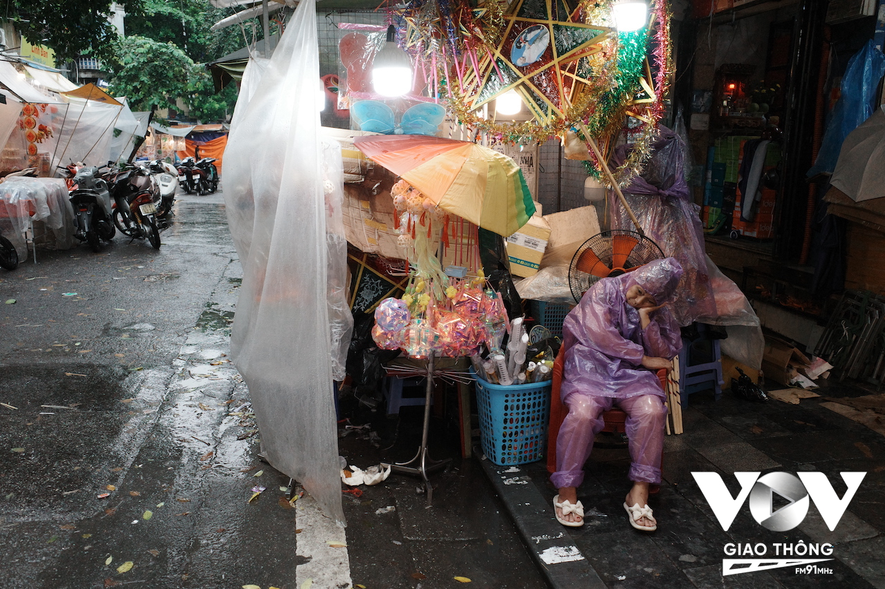 Một người bán hàng ủ rũ trong cơn mưa bên quầy hàng trên phố Hàng Mã