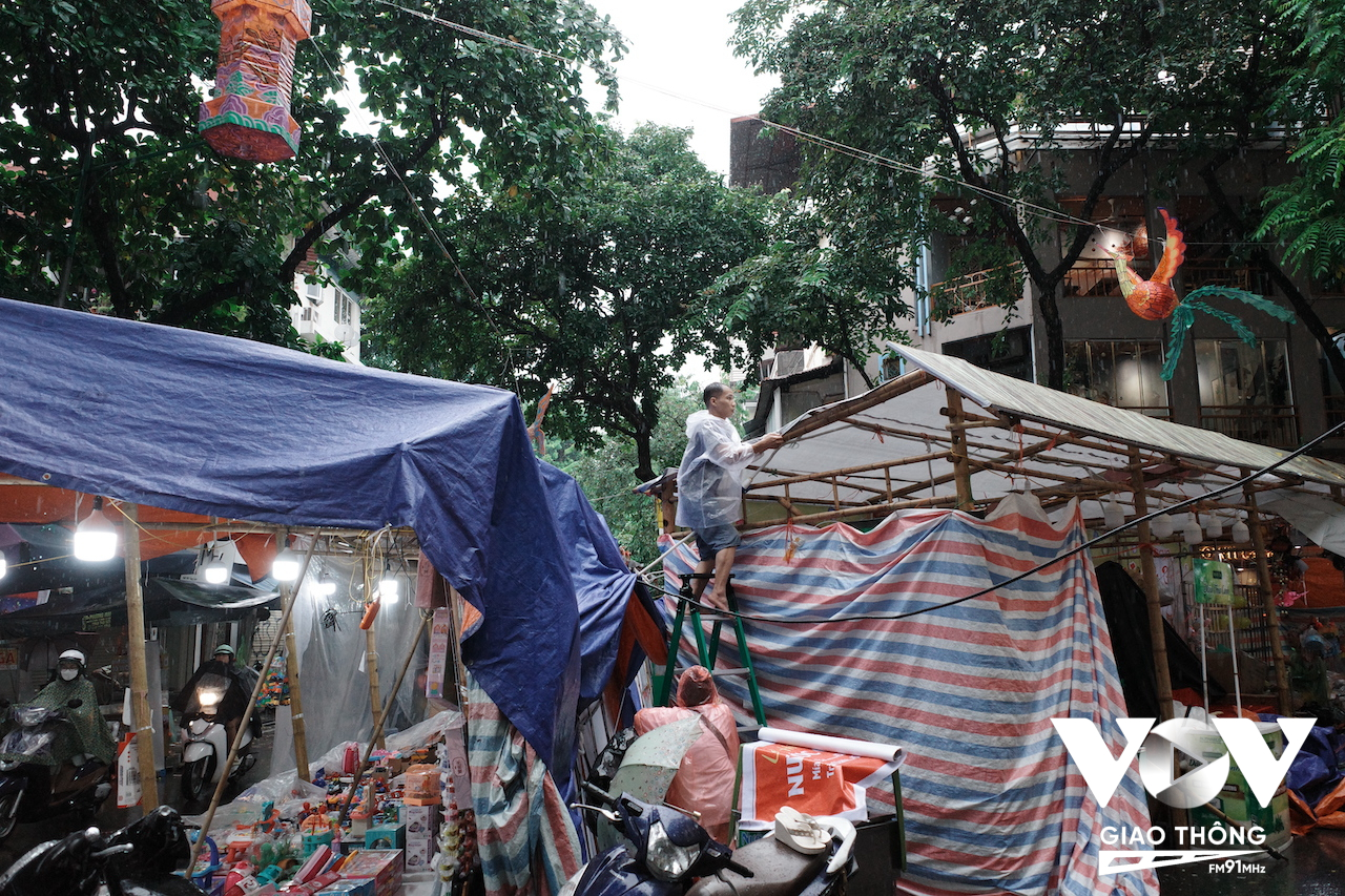 Một người bán hàng đang gia cố lại mái che cho quầy hàng của mình để tránh mưa
