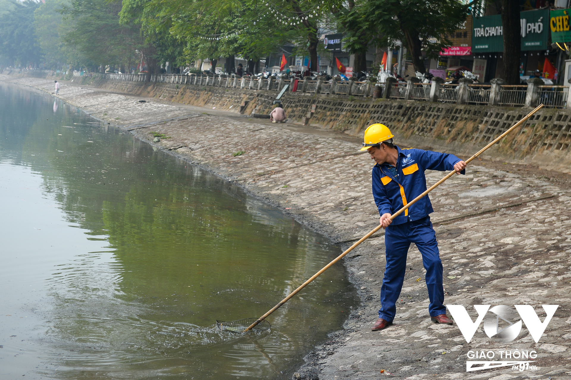Để đảm bảo vệ sinh môi trường, công nhân Xí nghiệp quản lý duy trì hồ trực thuộc Công ty TNHH MTV Thoát nước Hà Nội vớt rác sau khi người dân thả cá tại hồ Hoàng Cầu. (Ảnh: Phúc Tài)