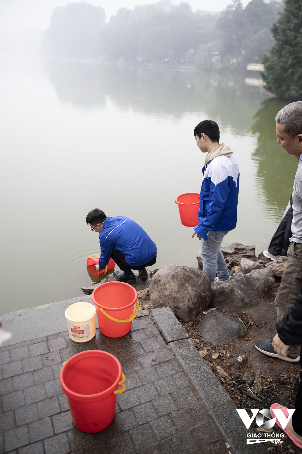 Một nhóm thanh niên tình nguyện mang xô, chậu để ở điểm thả cá để người dân mang cá đến bỏ vào rồi xách xuống hồ thả giúp cho những người lớn tuổi không thể đi xuống sát mép hồ...(Ảnh: Quang Hùng)