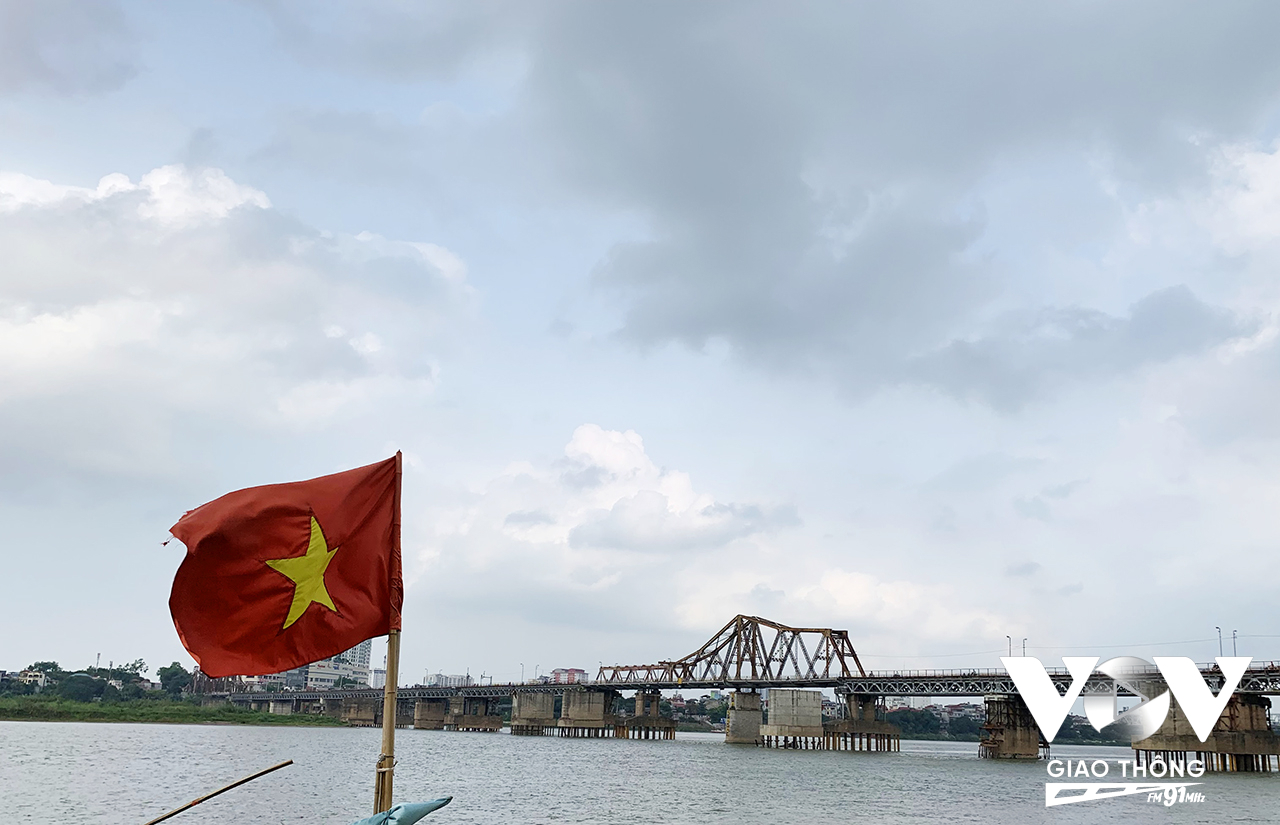 Một lá cờ tung bay trong gió sông Hồng, xa xa là cây cầu Long Biên, nơi chứng kiến những thời khắc quan trọng của Thủ đô và đất nước