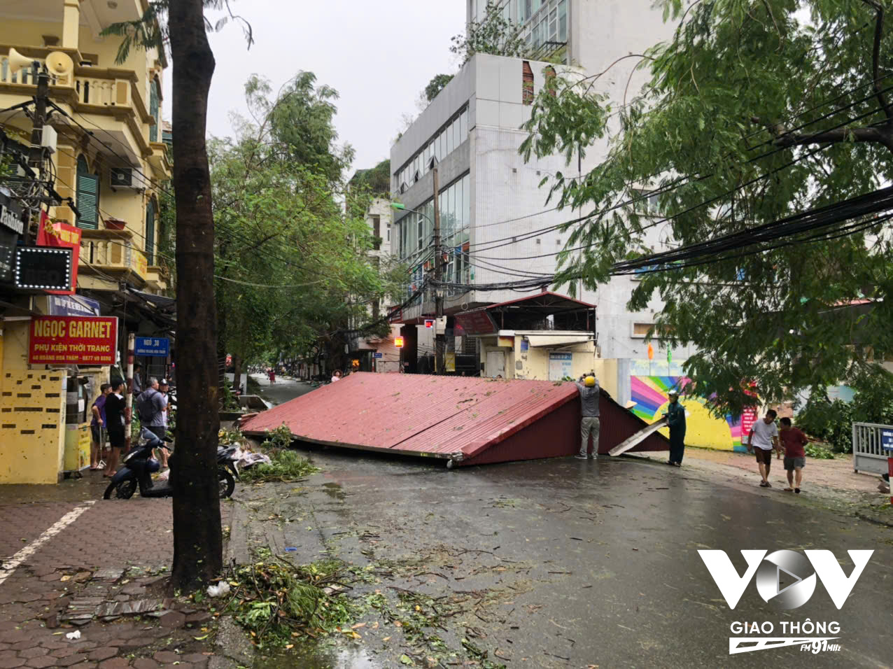 Tạm cấm ô tô di chuyển vào Hoàng Hoa Thám đoạn từ dốc Tam Đa về Ngọc Hà. Cổng nhà máy bia có cây đổ chắn ngang đường. Cổng trường THCS Ba Đình nguyên mái tôn bay xuống từ đêm qua đang được tháo dỡ (Ảnh: Nguyễn Minh)