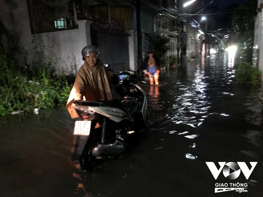 Một con hẻm bị ngập kèm mưa khiến người dân di chuyển khó khăn