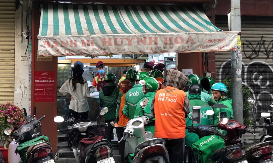 Tài xế xếp hàng chờ nhập đồ ăn đi giao tại một tiệm bánh mì ở quận 1, TP HCM ngày 15/2. Ảnh: Vnexpress