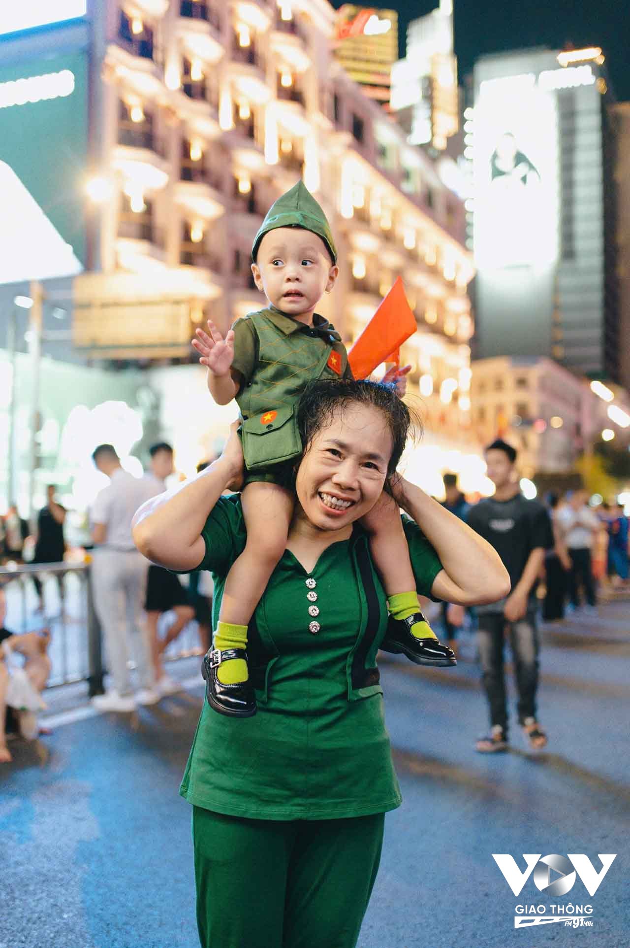 Nhiều gia đình mang theo con nhỏ, những em bé được bố mẹ công kênh trên vai, tay cầm lá cờ đỏ sao vàng nhỏ xinh, háo hức