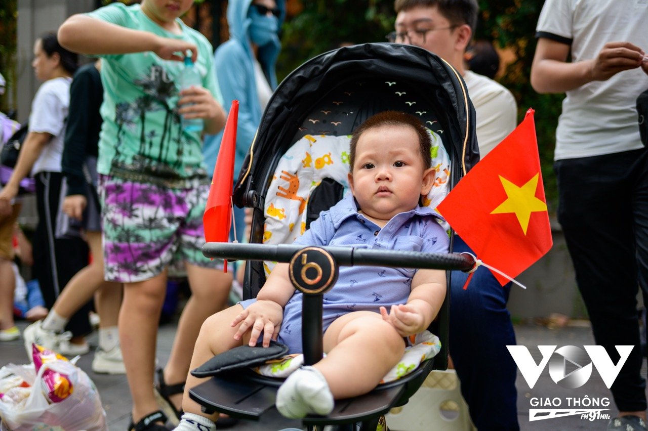 Một em bé cùng lá cờ Tổ quốc được bố mẹ đưa đi theo dõi buổi sơ duyệt diễu binh, diễu hành cấp Nhà nước mừng Đại lễ 30/4